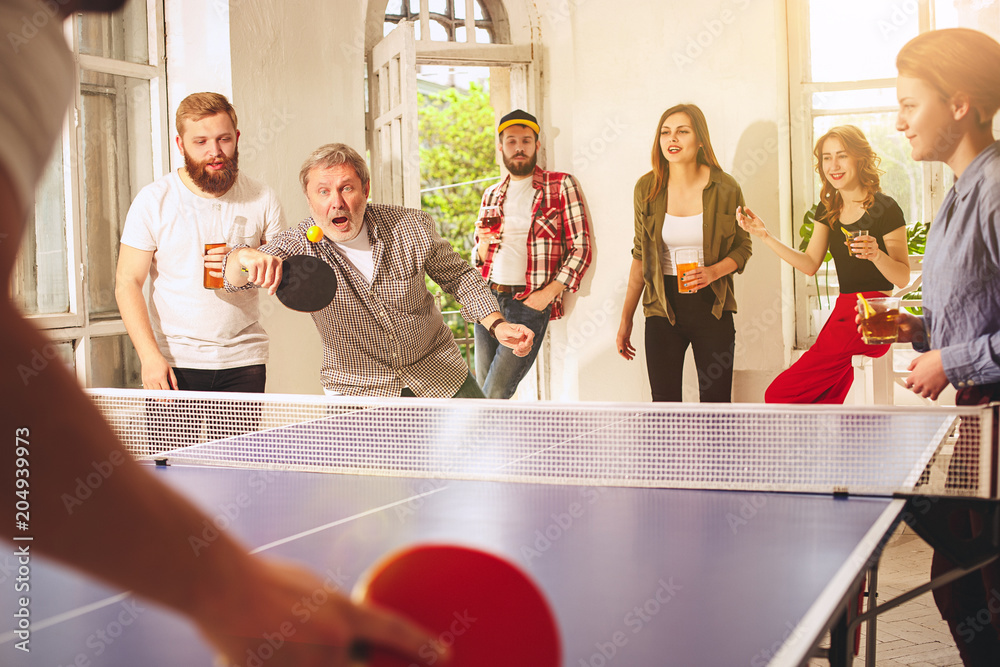 Obraz premium Group of happy young friends playing ping pong table tennis