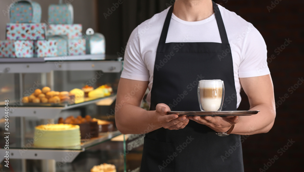 Young waiter holding tray with glass of coffee at workplace Young waiter holding tray with glass of coffee at workplace