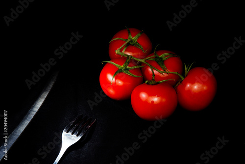 fresh ripe tomatoes red fork and knife black background photo