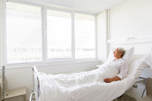 medicine, healthcare and old people concept - sad senior woman lying on bed at hospital ward photo
