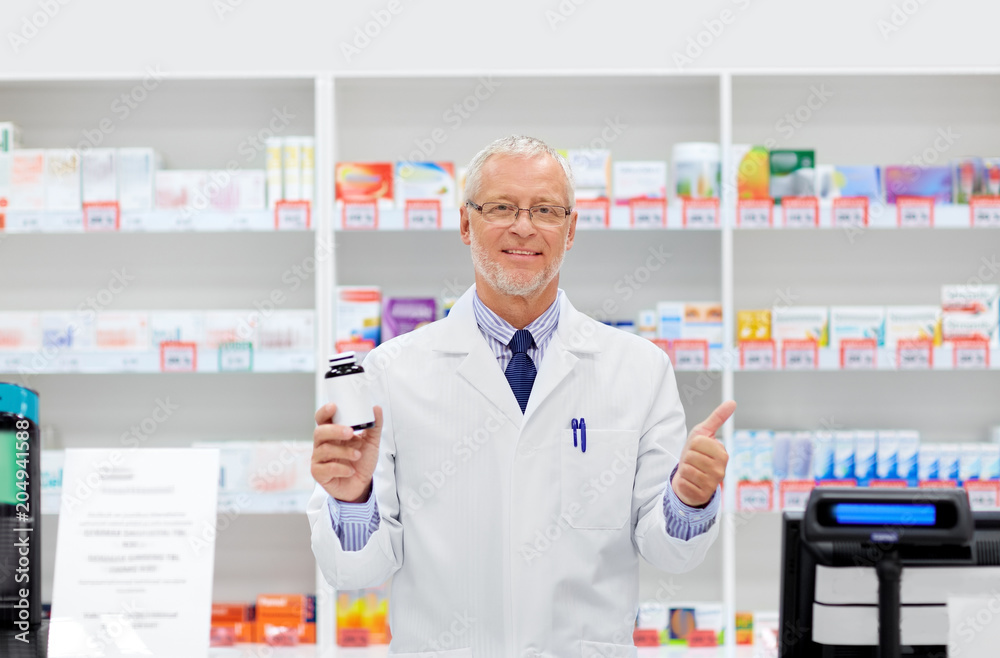 medicine, healthcare and people concept - senior apothecary with drug at pharmacy cash register showing thumbs up