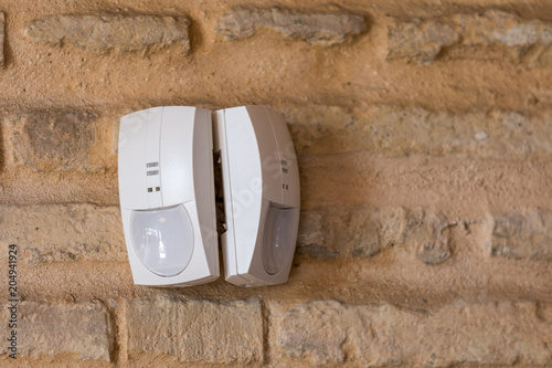 Milan, Italy - April 25, 2018: two alarm pir sensors installed on a face-facing brick wall photo