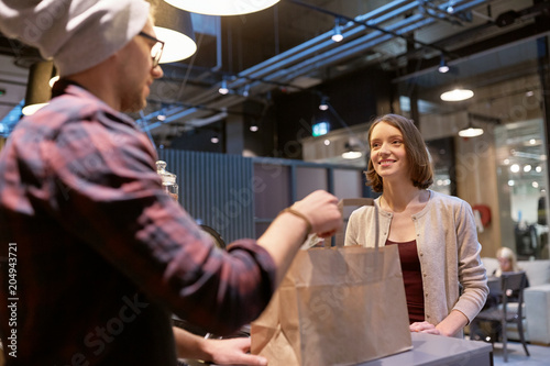 small business, takeaway food, people and service concept - man or seller giving paper bag and money change to happy female customer at vegan cafe