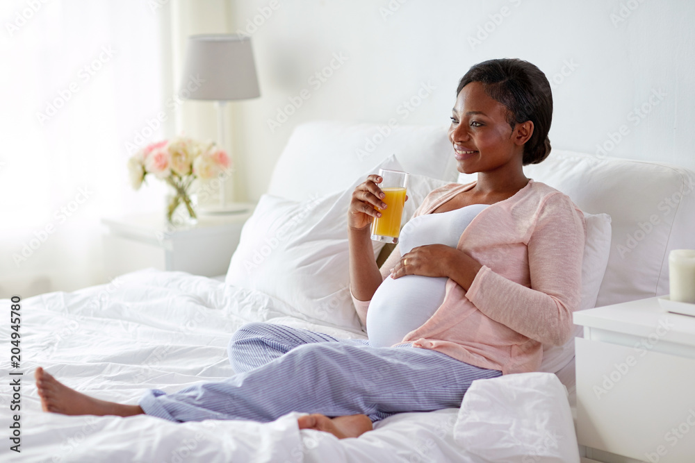 pregnancy, people and rest concept - happy pregnant african american woman drinking orange juice in bed at home pregnancy, people and rest concept - happy pregnant african american woman drinking orange juice in bed at home
