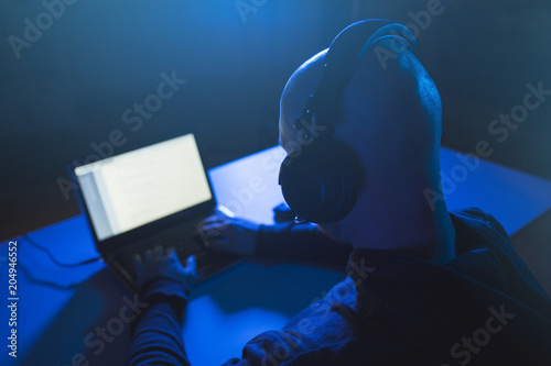 cybercrime, hacking and technology concept - male hacker with headset using laptop computer for cyber attack or wiretapping in dark room photo