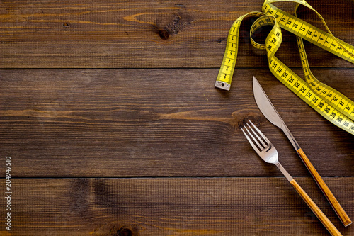 Proper nutrition for slimming. Fork, knife and measuring tape on dark wooden background top view copy space