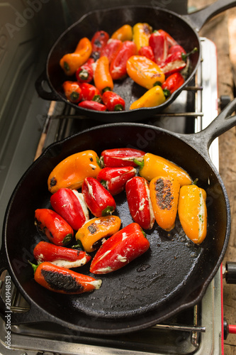 Seared peppers stuffed with cheese prepared in cast iron pan during camping trip