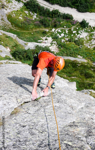 rock climber dressed in bright colors on a steep granite climbing route in the Alps photo