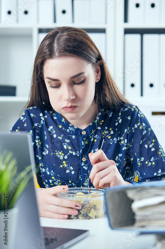 Business woman eating lunch at her workplace looking at the laptop screen. Folders with documents in the foreground. photo