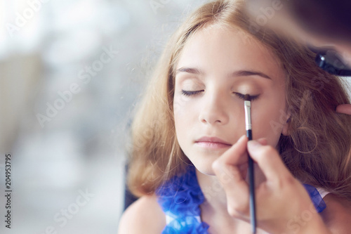 Stylist doing the make-up for a beautiful little girl model.