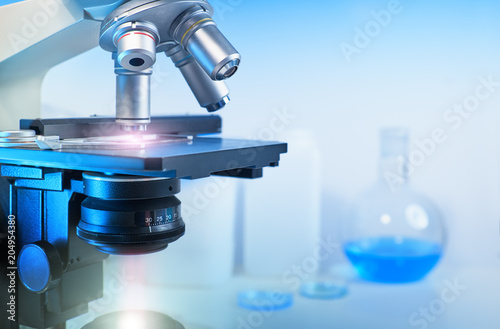 Scientific background with closeup on light microscope and laboratory out of focus