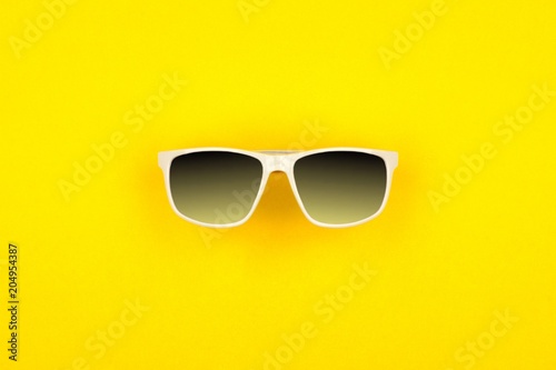 Sunglasses with bright yellow background. Top view, minimal summer concept.