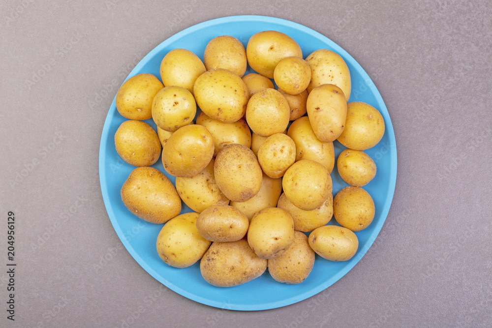 Fresh potatoes lie on a plate of turquoise color. The background is gray. Top view. Fresh potatoes lie on a plate of turquoise color. The background is gray. Top view.