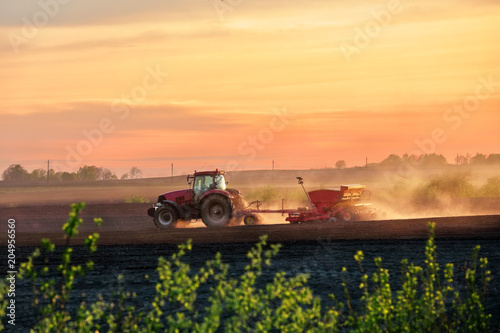 A red tractor with a seeder on a cultivated field in the spring at sunset photo