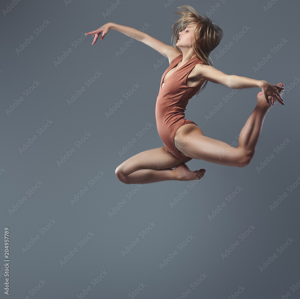 Young graceful ballerina dances and jumps in a studio. Isolated on a gray background.