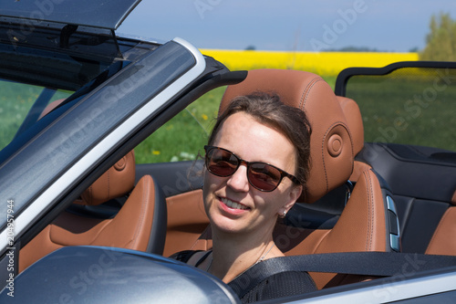 Beautiful happy brunette woman with sunglasses driving a Luxury Convertible Sports Car on a sunny day