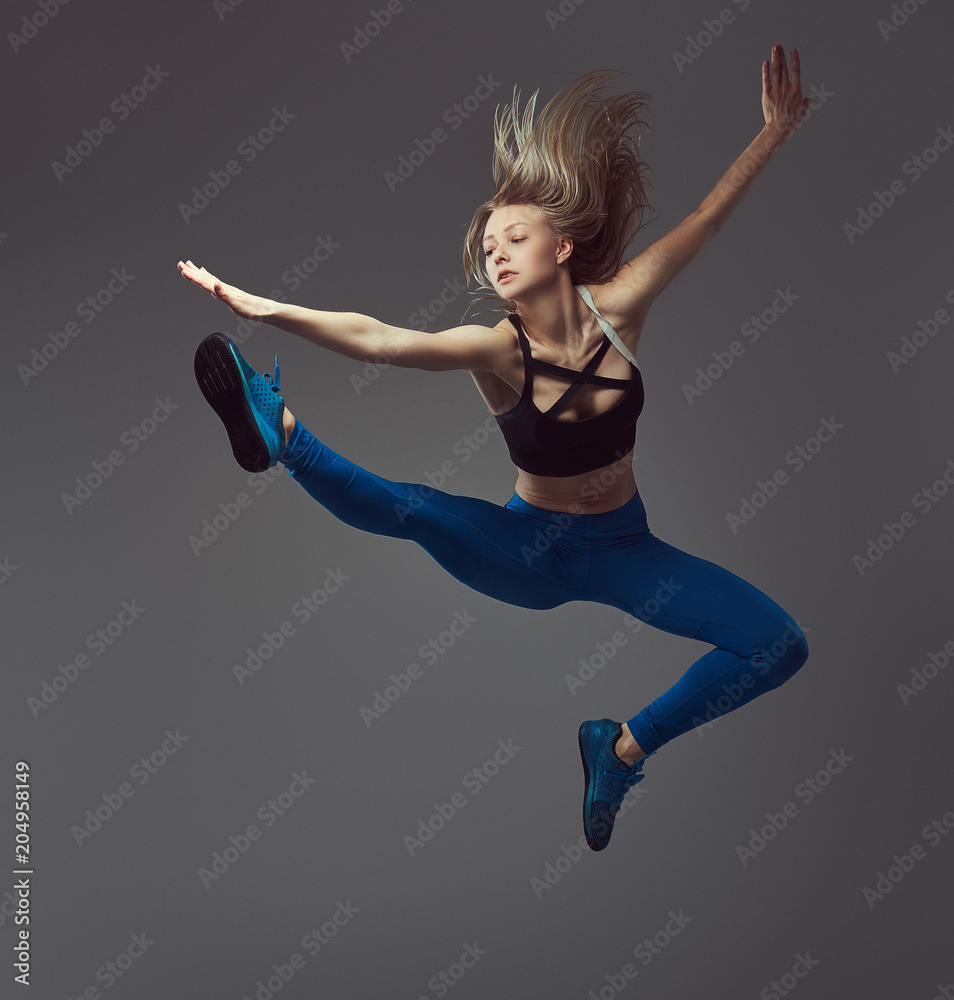Fototapeta premium Young ballerina in sportswear dances and jumps in a studio. Isolated on a gray background.