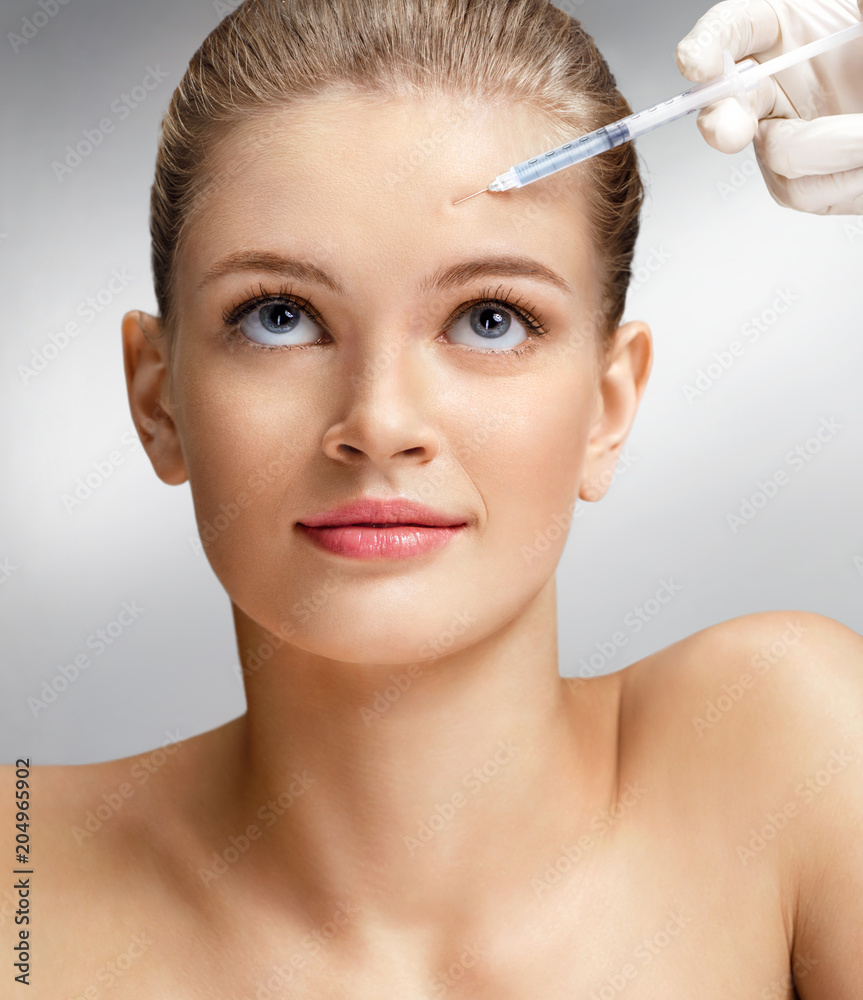 Beautiful woman face and beautician hands with syringe makes cosmetic injection in forehead. Clean Beauty concept