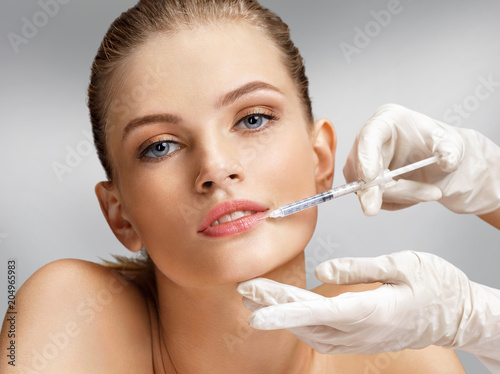 Beautiful woman face and beautician hands with syringe makes cosmetic injection in the upper lip. Clean Beauty concept