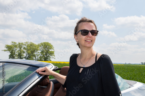 Beautiful happy brunette woman with sunglasses with her new Luxury Convertible Sports Car on a sunny day © Riko Best