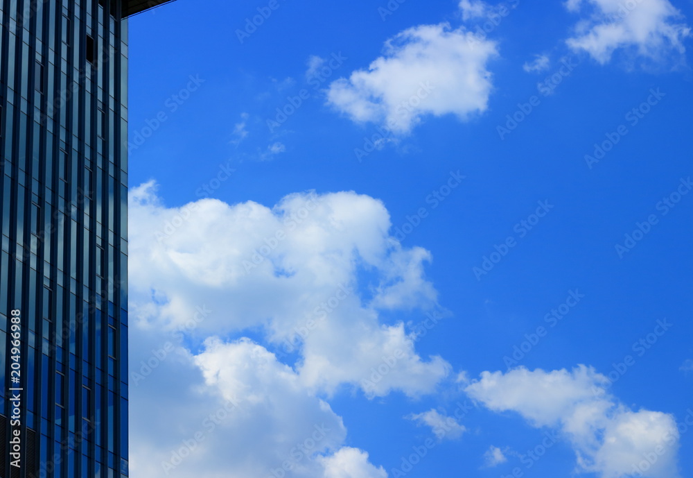 Landscape of part glass wall of a modern building on a background of a bright blue sky with amazing clouds. Background of a modern cityscape with reflection sky in the skyscraper Landscape of part glass wall of a modern building on a background of a bright blue sky with amazing clouds. Background of a modern cityscape with reflection sky in the skyscraper