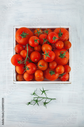 box of fresh ripe red tomatoes in different sizes on white wood kitchen table, can be used as background 