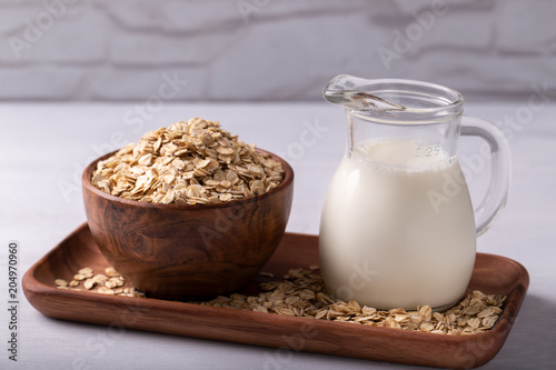 Vegan non dairy oat milk and flakes on white wooden background. Healthy eating