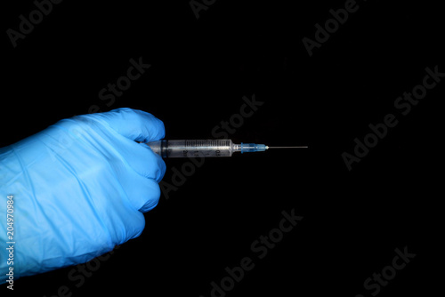 A doctor in blue gloves holds a syringe on an isolated black background. High resolution product photo