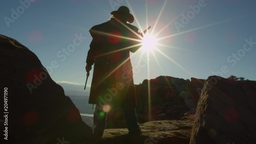 Cowboy standing with guns on desert cliff 