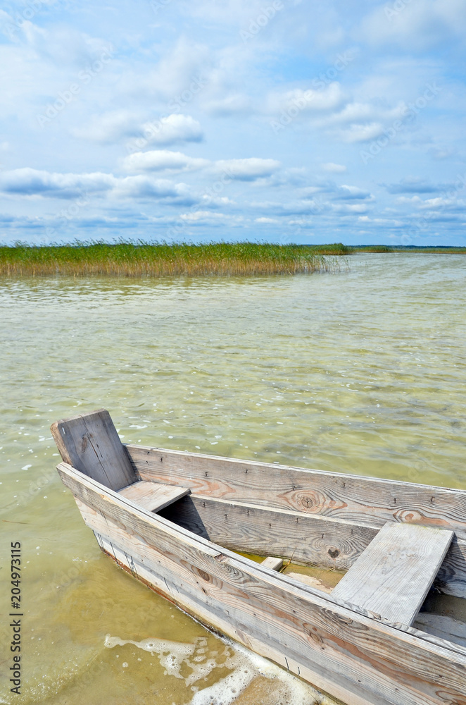 Wooden fishing boat on the lake beach with blue sky, yellow sand and transparent water