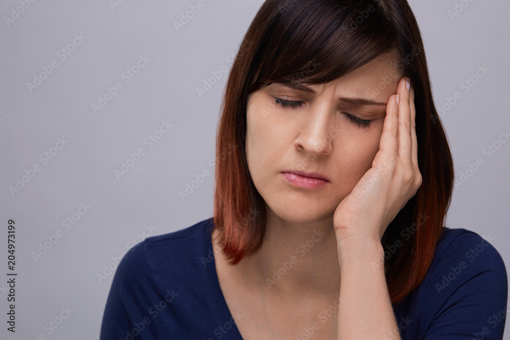 Closeup portrait of young woman on grey background suffering from strong headache, holding fingers to temples and closing eyes from pain.Severe migraine. Closeup portrait of young woman on grey background suffering from strong headache, holding fingers to temples and closing eyes from pain.Severe migraine.