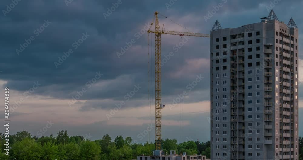Time lapse of silhouette of a tower crane working on construction with white fluffy curly rolling clouds as background in the evening Time lapse of silhouette of a tower crane working on construction with white fluffy curly rolling clouds as background in the evening