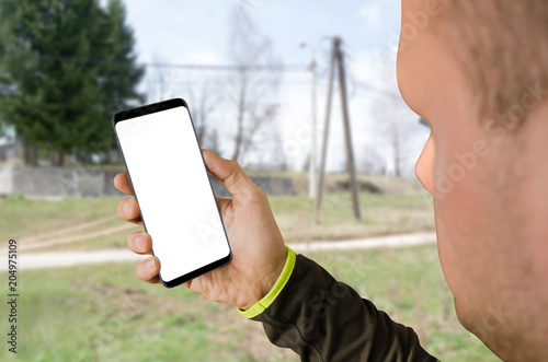 Modern smartphone with an isolated white screen for website or app mockup in a man's hand. Close up. City area in the background
