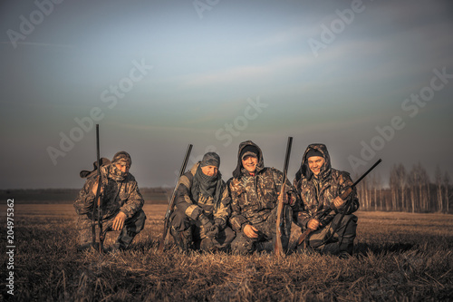 Men hunters group team portrait in rural field posing together against sunrise sky during hunting season. Concept for teamwork  friendship and brotherhood.