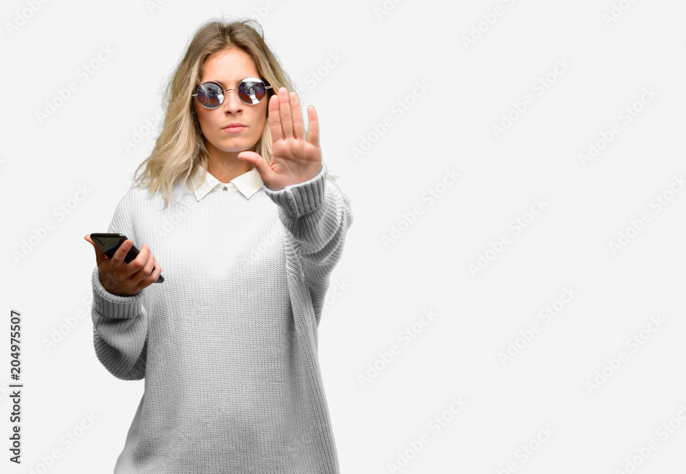 Young beautiful woman using smartphone annoyed with bad attitude making stop sign with hand, saying no, expressing security, defense or restriction, maybe pushing Young beautiful woman using smartphone annoyed with bad attitude making stop sign with hand, saying no, expressing security, defense or restriction, maybe pushing