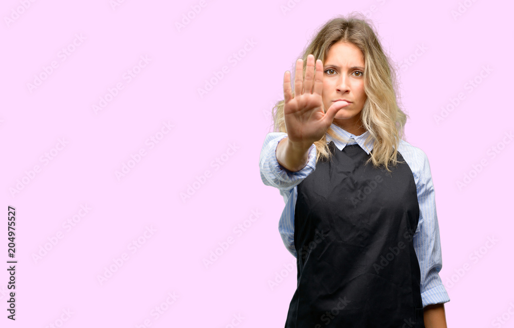 Young shop owner wearing black apron annoyed with bad attitude making stop sign with hand, saying no, expressing security, defense or restriction, maybe pushing Young shop owner wearing black apron annoyed with bad attitude making stop sign with hand, saying no, expressing security, defense or restriction, maybe pushing