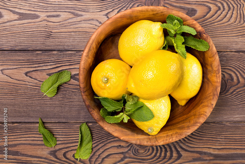 Fresh lemons in an olive bowl on a wooden background. In the style of rustic. Copy space. Top view of food.