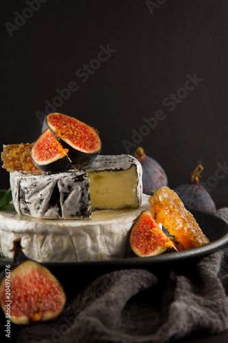 tasty camembert with fresh figs and honey with honeycombs, decorated on a plate on dark background, rustic, moody food photography