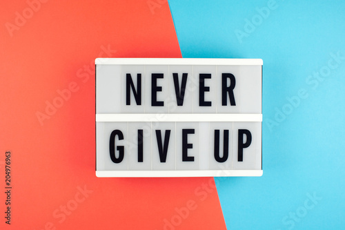 Never give up  - text on a display lightbox on blue and red bright background.