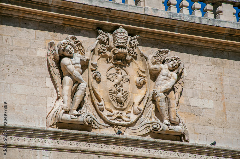 Detail of stone ornament of building in front of the Palace of the Popes of Avignon, under a sunny blue sky. Located in the Vaucluse department, Provence-Alpes-Côte d'Azur region, southeastern France