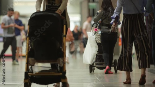 Anonymous young mothers shopping in a mall, walking and pushing strollers.