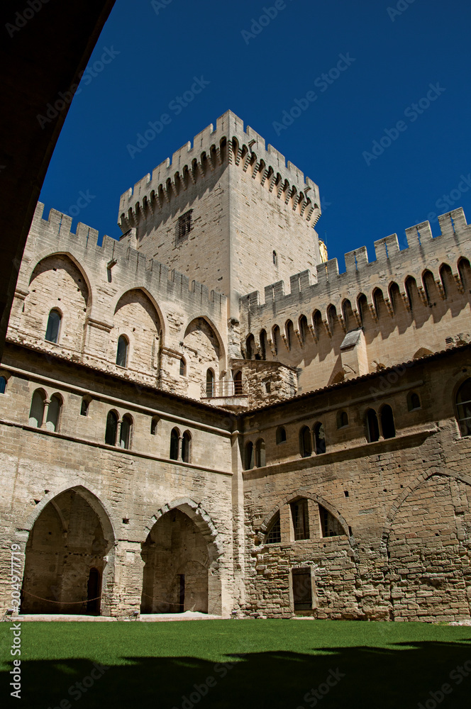 View of courtyard and internal buildings of the Palace of the Popes of Avignon, under a sunny blue sky. Located in the Vaucluse department, Provence-Alpes-Côte d'Azur region, southeastern France
