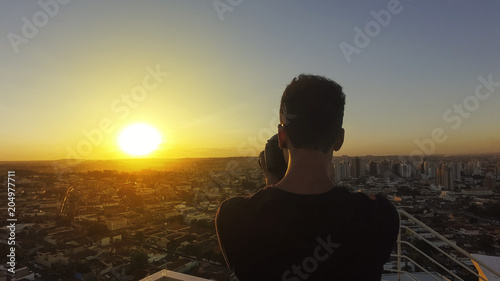 Canvas Print Silhouette of a photographer taking pictures on top of the building at sunset