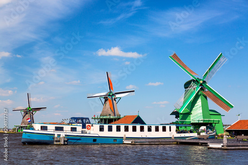 Dutch typical landscape. Traditional old dutch windmills with cruise ship and blue sky in the Zaanse Schans village, Netherlands. Famous tourism place.