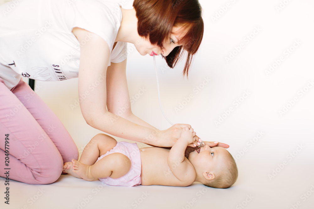 Mother using nasal aspirator for cute little baby lying on bed at home. Health care concept Mother using nasal aspirator for cute little baby lying on bed at home. Health care concept