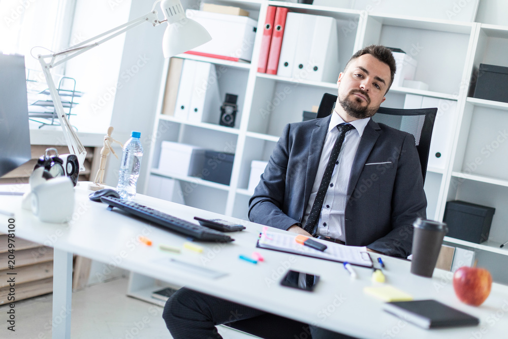 A man is sitting in a chair in the office at the table. A man is sitting in a chair in the office at the table.