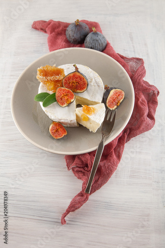 tasty camembert with fresh figs and honey with honeycombs, decorated on a white wood plate background, rustic, moody food photography