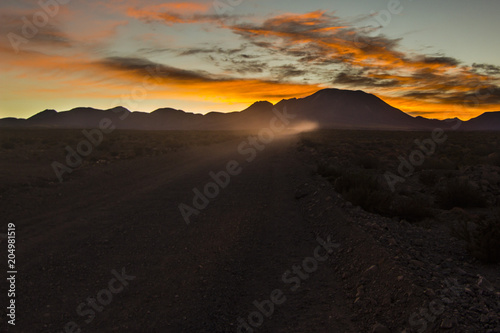 An off road vehicle traveling along the Atacama Desert heading Lascar Volcano when the sun is rising above the sky giving the first ray of lights, Chile