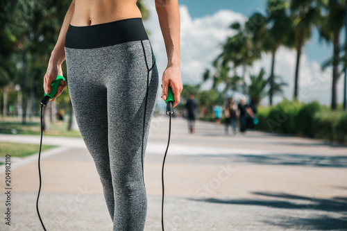 Close up of slender female legs standing on the road outdoor. Girl is holding a skipping rope. Copy space