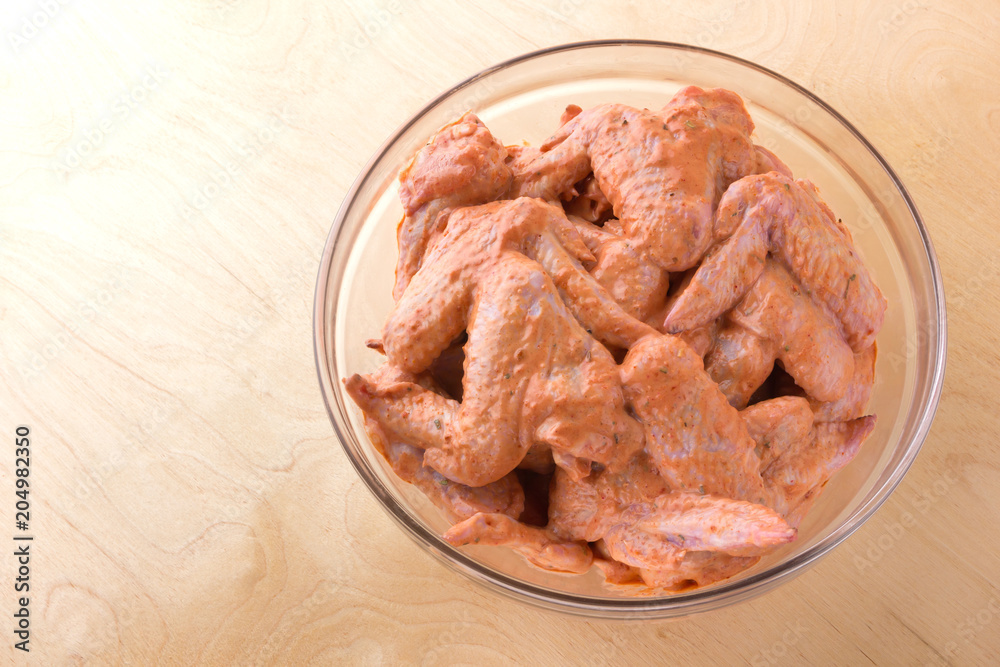 Marinated chicken wings in a glass bowl. Glass dish with marinated wings on a wooden table. Marinated chicken wings in a glass bowl. Glass dish with marinated wings on a wooden table.
